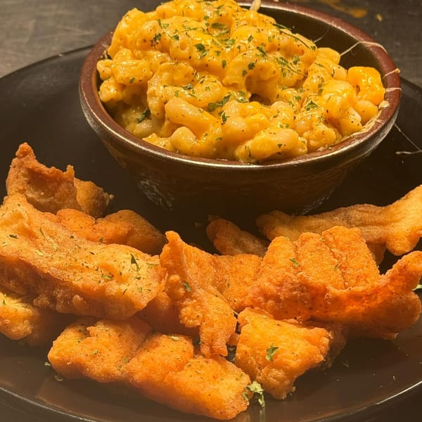 A bowl of creamy mac and cheese with parsley next to a pile of crispy fried chicken.