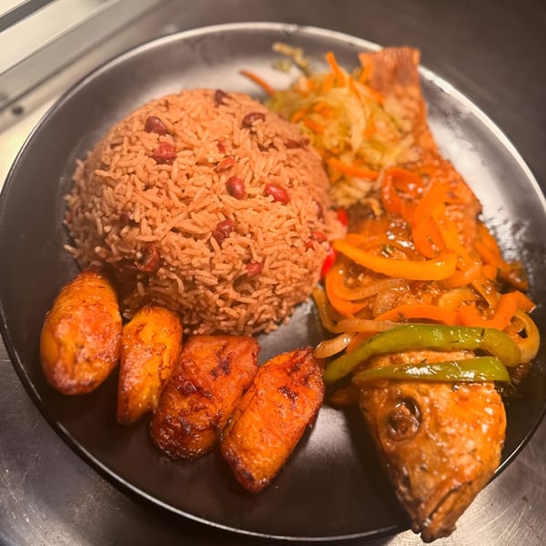 Haitian fried fish with rice and beans, plantains, and pickled vegetables on a black plate.