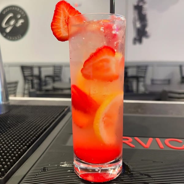A tall glass of strawberry lemonade with lemon slices and a strawberry garnish on a bar.