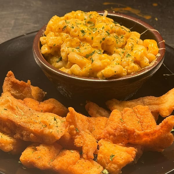 A bowl of creamy mac and cheese with parsley, next to a pile of golden-fried chicken pieces.